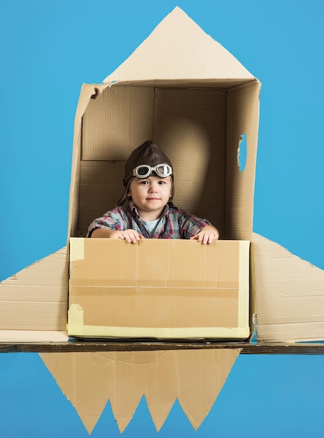 Menino brincar no foguete. conceito de infância. criança no foguete de papelão de brinquedo. sonho de infância. astronauta. conceito de cosmonauta. espaço. isolado em um fundo azul.