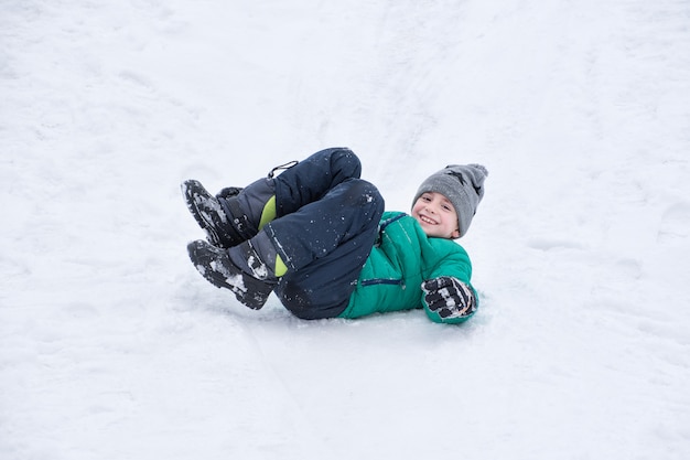 Menino cai rolando uma colina de neve.