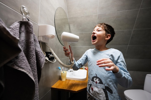 Menino cantando com um secador de cabelo no banheiro