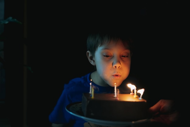 Menino caucasiano bonitinho fazendo um desejo soprando velas no bolo em seu aniversário de 9 anos