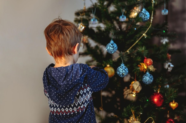 Menino caucasiano bonito decorando a árvore de Natal com decorações cintilantes