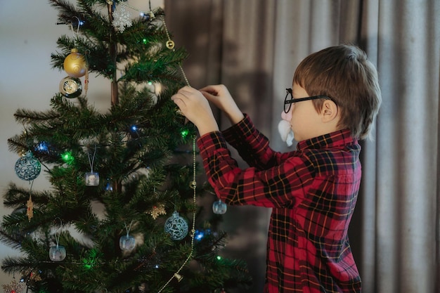 Menino caucasiano bonito decorando a árvore de Natal com decorações cintilantes