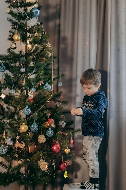 Menino caucasiano bonito decorando a árvore de Natal com decorações cintilantes