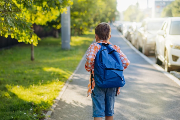 Foto menino caucasiano caminhando para a escola vestindo saco escolar no início do ano acadêmico