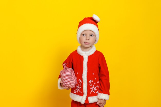 Menino caucasiano de três anos com uma fantasia festiva de Papai Noel segurando uma sacola com presentes