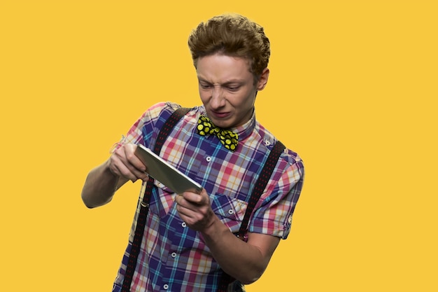 Menino caucasiano está jogando no smartphone. Schoolboy está segurando um dispositivo para jogos. Isolado em fundo amarelo.