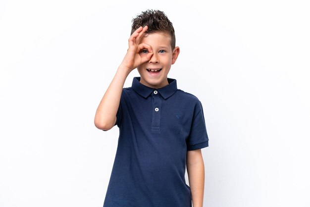Foto menino caucasiano isolado no fundo branco, mostrando sinal de ok com os dedos