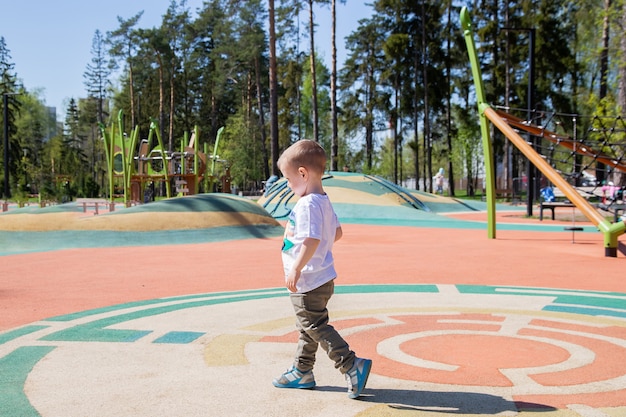 Menino caucasiano percorre o território do playground ao ar livre em um dia ensolarado.