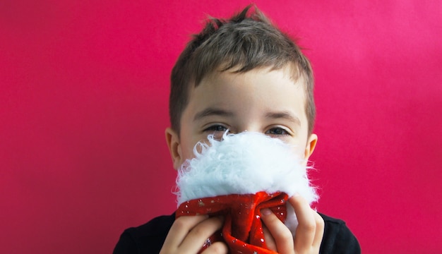 Menino caucasiano se esconde atrás de um chapéu de Papai Noel rosa