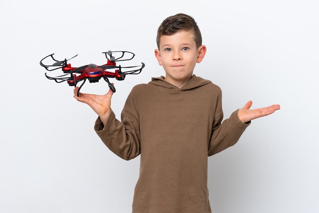 Menino caucasiano segurando um drone isolado no fundo branco com dúvidas ao levantar as mãos