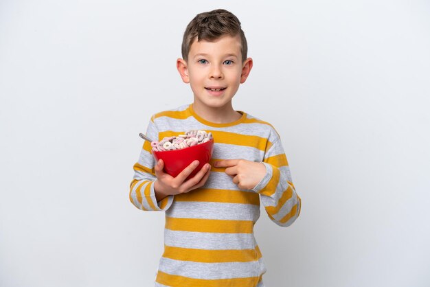 Menino caucasiano segurando uma tigela de cereal isolada no fundo branco com expressão facial de surpresa