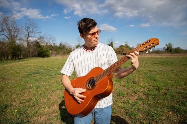 Menino caucasiano toca violão ao ar livre em um campo Músico toca um instrumento