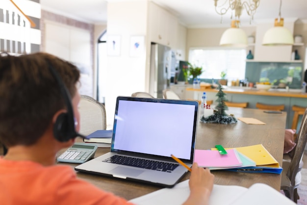 Menino caucasiano usando laptop com espaço para cópia e fones de ouvido em casa