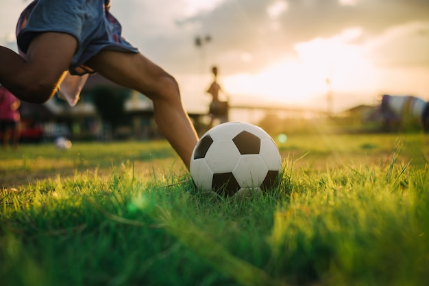 Menino chutando uma bola com o pé descalço enquanto jogava futebol de rua no campo de grama verde