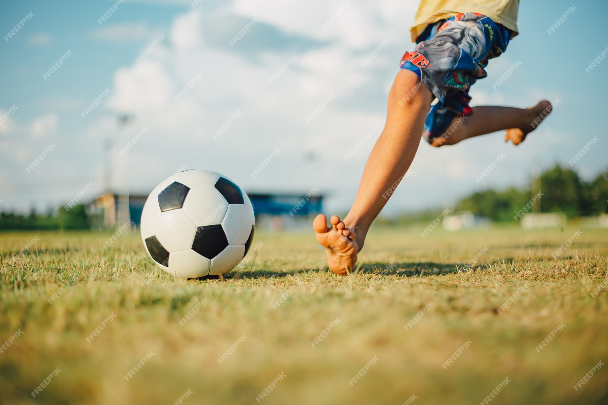 Garoto Joga Bola De Futebol Na Praia Arenosa. Pés Descalços De