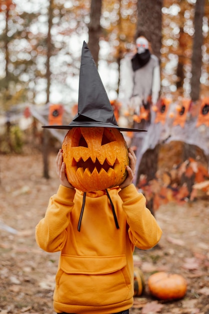 Menino com abóbora de halloween no chapéu de bruxa preta Menino se divertindo celebrando o conceito de halloween