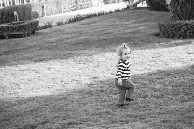 Menino com cabelo loiro corre na grama verde