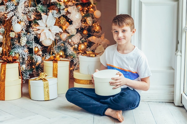 Foto menino com caixa de presente perto da árvore de natal