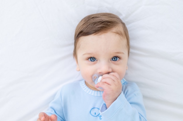 Menino com chupeta na cama antes de ir para a cama com macacão azul, bebezinho feliz e saudável