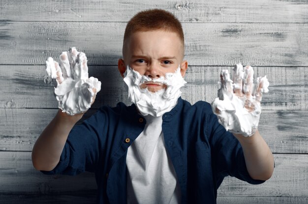 Menino com espuma de barbear no rosto e as mãos em estúdio.