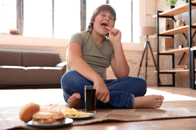 Menino com excesso de peso com fast food em casa