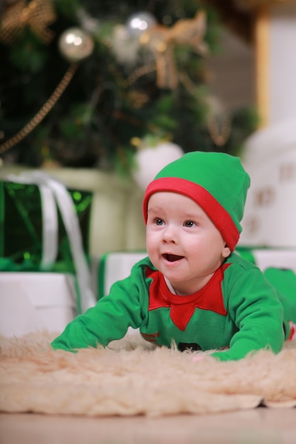 Foto menino com fantasia de elfo verde vermelho sentado sob a árvore de natal e caixas de presente.