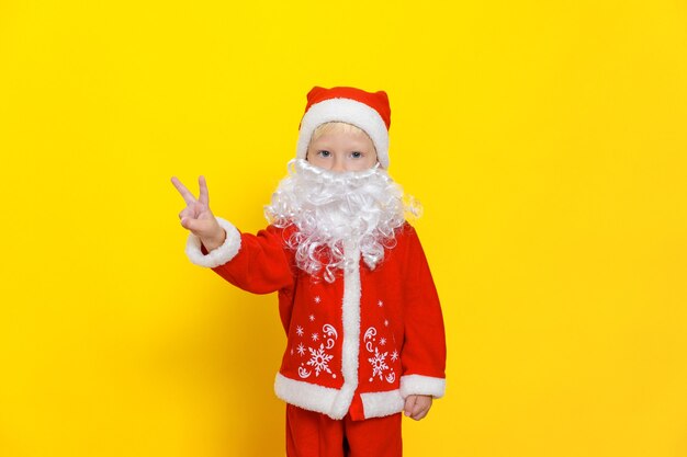 Menino com fantasia de Natal vermelha com barba branca mostra gesto de vitória com as mãos