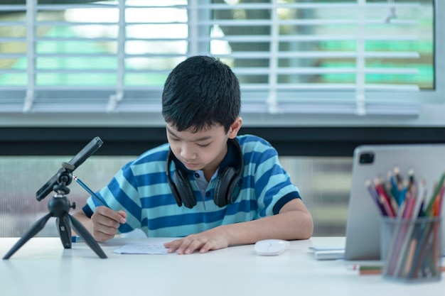 Foto menino com fones de ouvido está usando um tablet e se comunica pela internet em casa