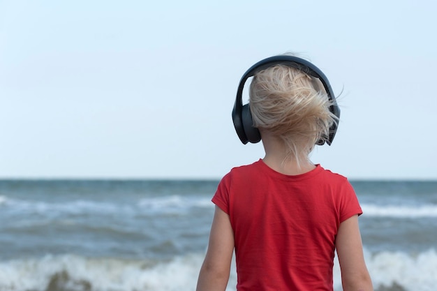 Menino com fones de ouvido olha para o mar e ouve música Relax Back view