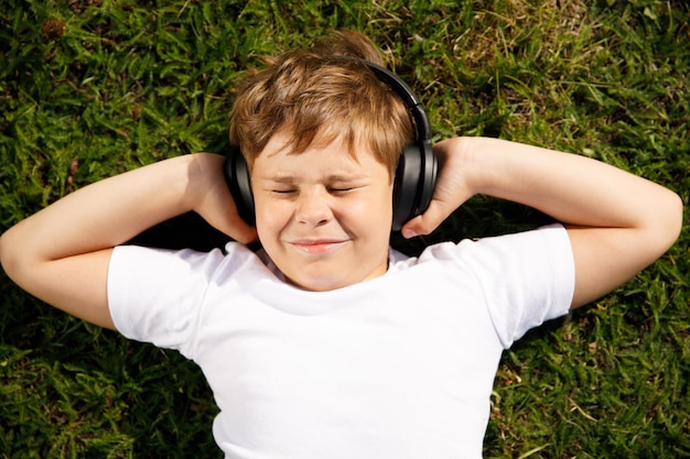 Menino com fones de ouvido, ouvindo música, deitado na grama