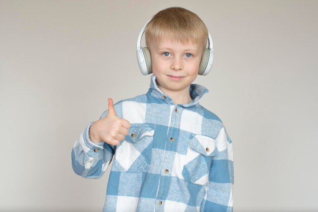 Foto menino com fones de ouvido ouvindo música e mostrando os polegares em fundo cinzento