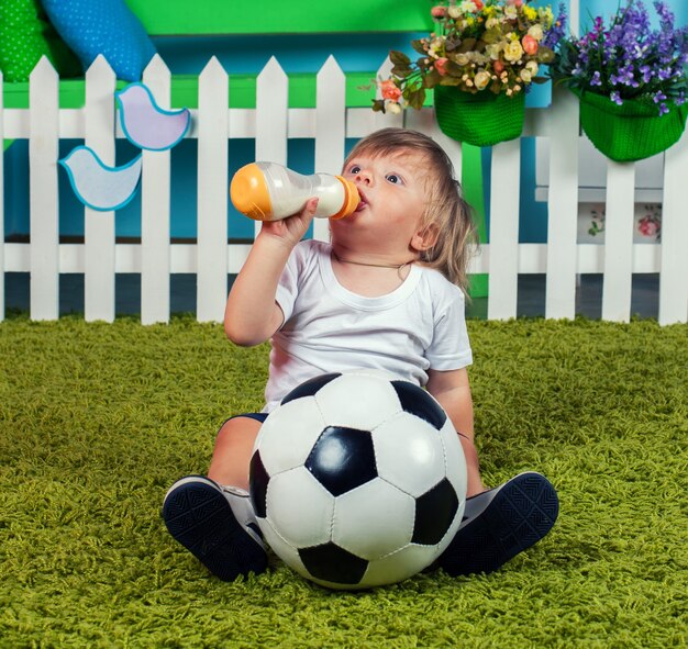 Foto menino com futebol bebendo leite da mamadeira com bico