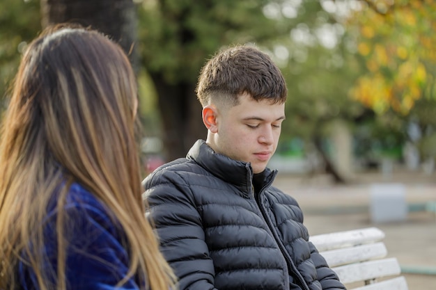 Menino com gesto melancólico sentado num banco da praça ao lado de uma menina