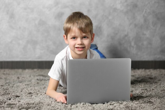 Menino com laptop no tapete de pele contra a superfície da parede cinza