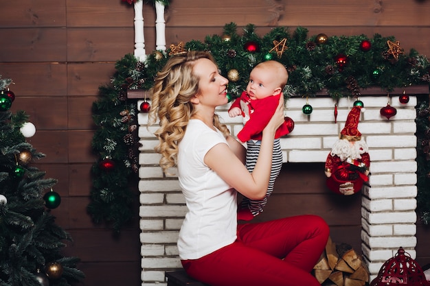 Menino com linda mãe loira abraçando na casa decorada para o Natal