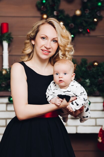 Menino com linda mãe loira abraçando na casa decorada para o Natal