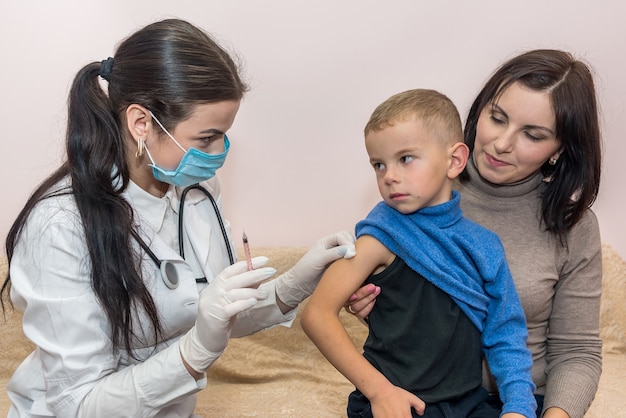 Menino com mãe e médico segurando uma seringa