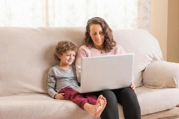 Menino com mãe usando laptop enquanto está sentado no sofá em casa