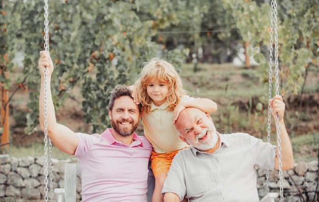 Menino com pai e avô balançando juntos no parque ao ar livre três gerações diferentes a