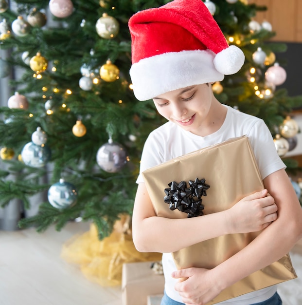 Menino com presentes brinca perto da árvore de natal. interior da sala de estar com árvore e decorações de natal. ano novo. doação de presente.