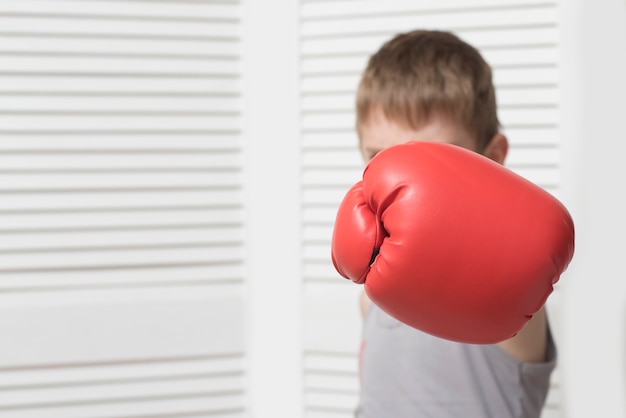 Menino com raiva na luva de boxe vermelha. Acertar