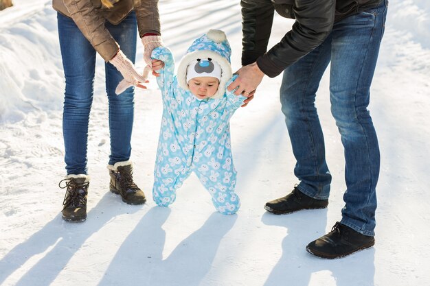 Menino com roupa de neve quente, caminhando no parque de inverno com os pais. Primeiro inverno e primeiros passos da criança na neve.