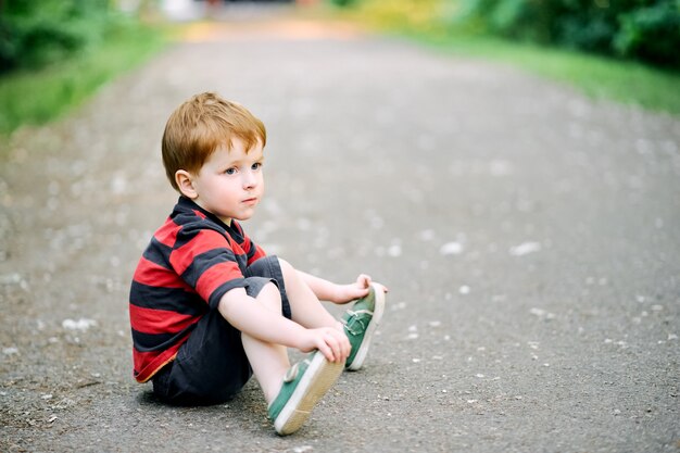 Foto menino com roupas casuais sentado no chão no verão no parque