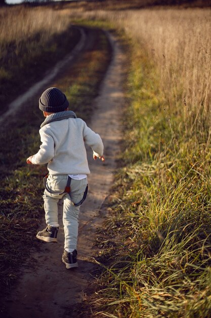 Menino com roupas quentes corre ao longo de um caminho em um campo com grama seca no outono