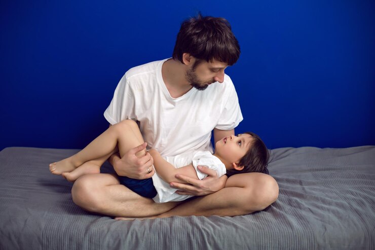 Foto menino com seu pai em camisetas brancas deitado em casa em uma cama contra uma parede azul