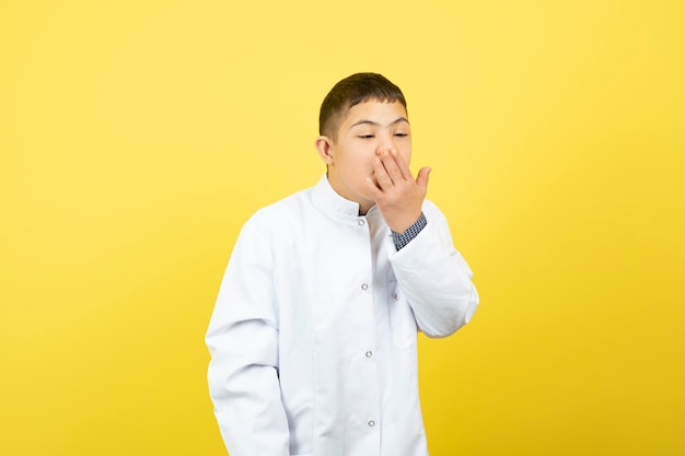 menino com síndrome de down, tossindo sobre uma parede amarela.