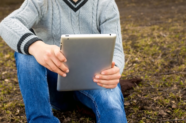 Menino com tablet nas mãos dele senta-se na grama