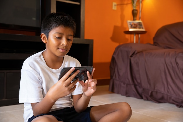 Menino com telefone celular em casa sentado em uma esteira em casa