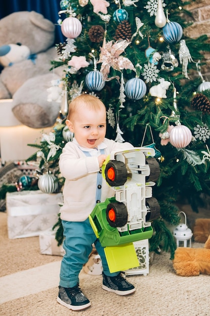 Menino com um brinquedo perto da decoração e da árvore de Natal