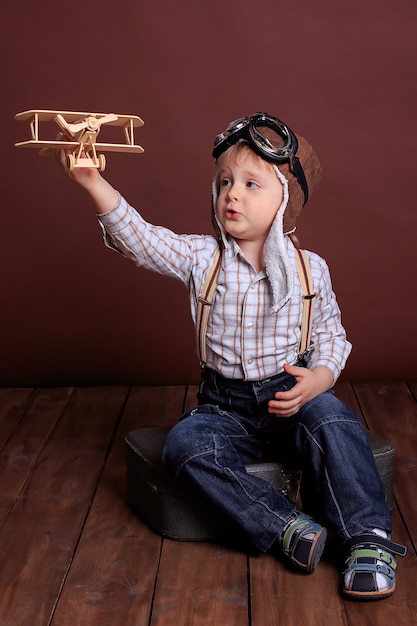 Menino com um capacete brinca com um avião de madeira. O menino sonha em se tornar piloto. Feriado dos homens